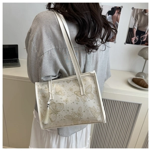 Detail of elegant beige tote bag with gold butterfly print and stylish white tassel charm