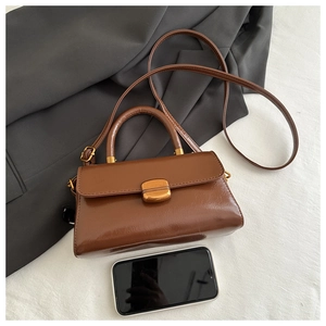 Mini brown leather crossbody bag with gold twist lock shown next to a smartphone
