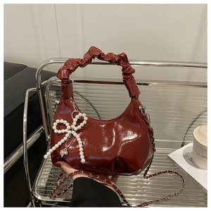 Detail of burgundy glossy pleated handbag with silver chain and pearl bow charm