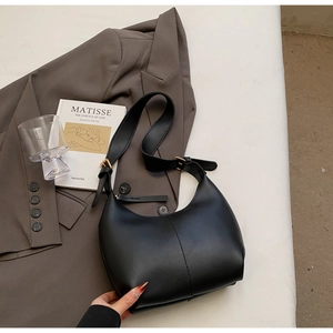 Close-up of black leather hobo bag with gold buckle on a stylish minimalist background