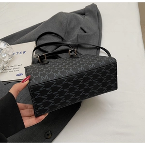 Detailed side view of black Boston bag featuring M letter print and gold hardware