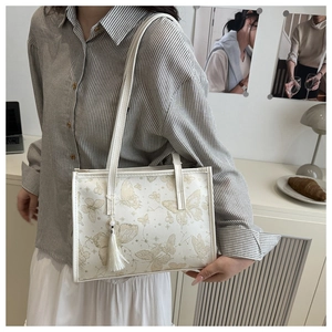 Detail of a beige tote bag featuring golden butterfly prints and a white tassel charm