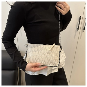 Detailansicht der Strohtasche mit silbernen Metallnieten und elegantem Kettenriemen