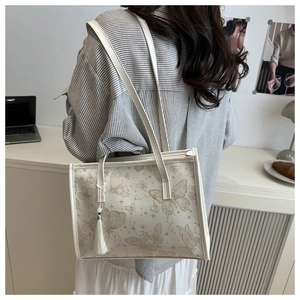 Chic cream tote bag with gold butterfly print and tassel detail shown on a shoulder