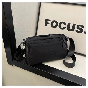 Detail of a black multi-zippered crossbody bag with wide fabric strap on a metal stand