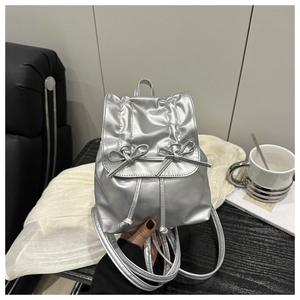 Detailed view of silver metallic mini backpack with ribbon bows on marble surface