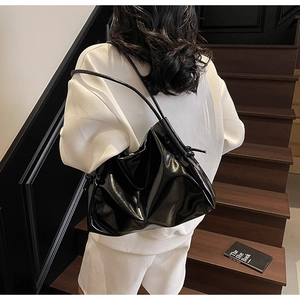 Detailed close-up of a glossy black tote bag featuring delicate knot strap accents