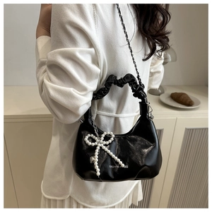 Detail of black glossy hobo bag with pearl bow pendant and silver chain strap