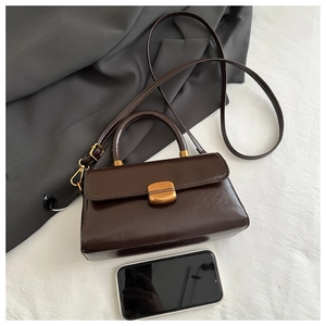 Top view of small vintage brown crossbody bag next to a smartphone for scale