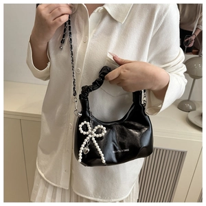 Détail du sac en cuir brillant noir avec pendentif nœud et poignée plissée chic