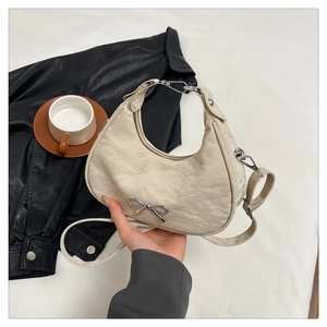 Detail of cream bow crescent bag with pleated texture and silver metallic bow detail