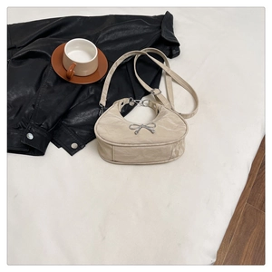 Detail of beige pleated crescent bag featuring a silver metal bow and adjustable strap