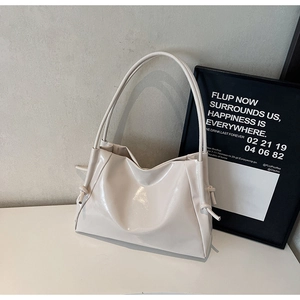 Close-up of beige glossy leather tote bag with knot detail and slim shoulder straps