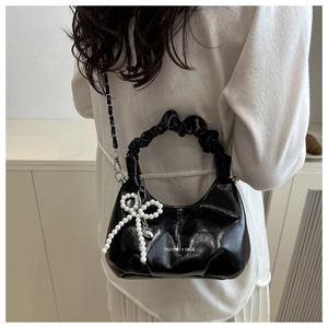 Detail of glossy black handbag with pearl bow charm and ruffled handle on white outfit