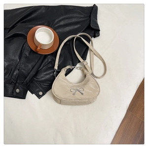 Detail of beige crescent shoulder bag featuring a metallic bow and adjustable strap