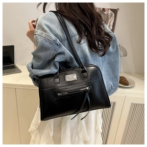 Detail einer schwarzen Handtasche mit Logo-Plakette und Quasten-Zippern an einem Model