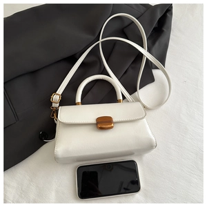 Mini white leather handbag with gold buckle shown next to a smartphone for size comparison