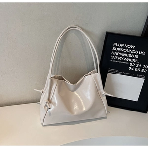 Detail of cream glossy leather tote bag featuring elegant side knot drawstring design