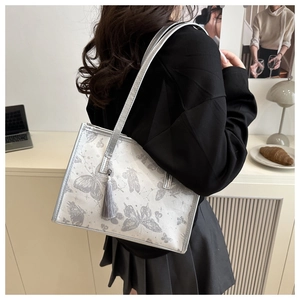 Detail of silver tote bag with butterfly patterns and grey silk tassel on model's shoulder