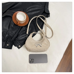 Flat lay of off-white bow crescent bag with silver metallic detail and long strap