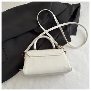 Detail of white textured leather crossbody bag with gold hardware on black blazer background