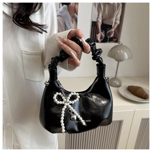 Detail of black crescent handbag featuring a ruched handle and pearl bow charm