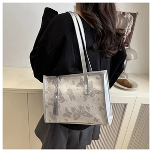 Silver tote bag with grey butterfly print and tassel detail shown in a home setting
