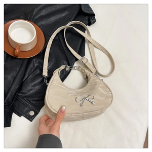 Close-up of cream quilted crescent bag featuring a silver bow buckle and top zipper