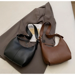 Detail of minimalist leather bucket bags in black and brown over a gray blazer