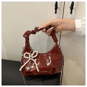 Detail of wine red patent leather handbag with pearl bow charm and chain strap