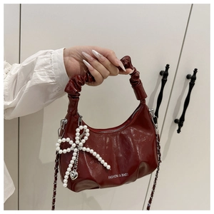 Detail of burgundy patent leather bag with pleated texture and pearl bow charm