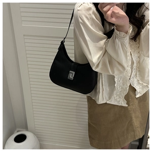 Detail of a minimalist black crescent shoulder bag with a silver metal clasp shown on a model