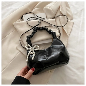 Detail of black pleated handle bag with silver chain and pearl bow charm on fabric