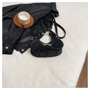 Macro view of black pleated hobo bag with a silver metal bow accent on white background