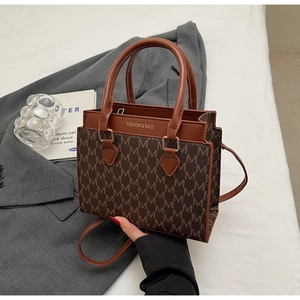 Detailansicht der braunen Monogramm-Umhängetasche mit Goldtext auf grauem Blazer