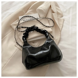 Detail view of black glossy handbag with pleated handle and slim metal chain strap