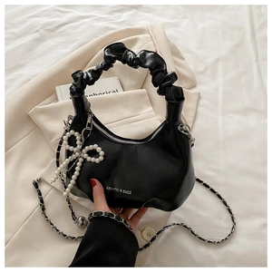 Black pleated handbag with pearl bow pendant and metal chain strap on a chic blazer
