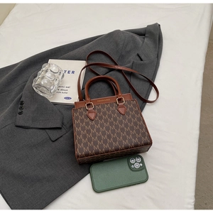 Draufsicht einer braunen Monogramm-Umhängetasche auf grauem Blazer und weißer Bettwäsche im Detail