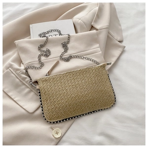 Detail der Stroh-Clutch mit silbernen Nieten und Metallkette auf hellem Blazer