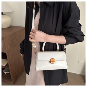 Close-up of a white leather crossbody bag featuring a golden metal twist-lock buckle detail
