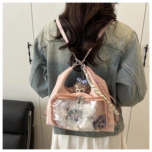 Pink ita bag with clear window showing lace details and character badges on denim jacket