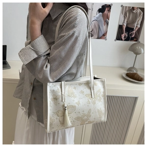 Detail of off-white tote bag with gold butterfly pattern and elegant tassel accessory