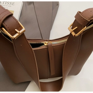 Detail view of smooth dark brown leather texture and golden metal zipper of the tote bag