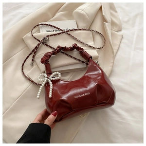 Detail of burgundy ruched faux leather handbag featuring a white pearl bow charm