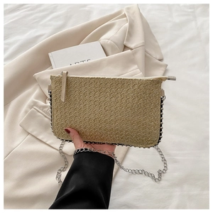 Detail der beigen Stroh-Clutch mit silbernem Perlenbesatz und zarter Gliederkette in der Hand