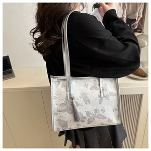 Close-up of pearl silver tote bag with grey butterfly print and beaded tassel charm