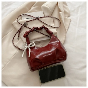 Close-up of deep red pleated leather handbag with pearl bow charm and chain strap