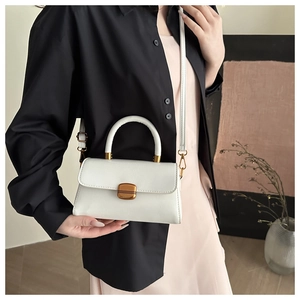 Close-up of a white leather crossbody bag with gold metal clasp and circular handle