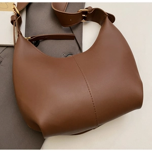 Close-up of brown leather crescent tote bag with adjustable strap and golden buckle