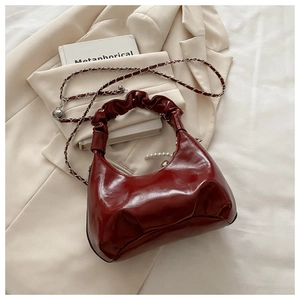 Close-up of a dark red pleated leather handbag featuring a pearl charm and chain strap
